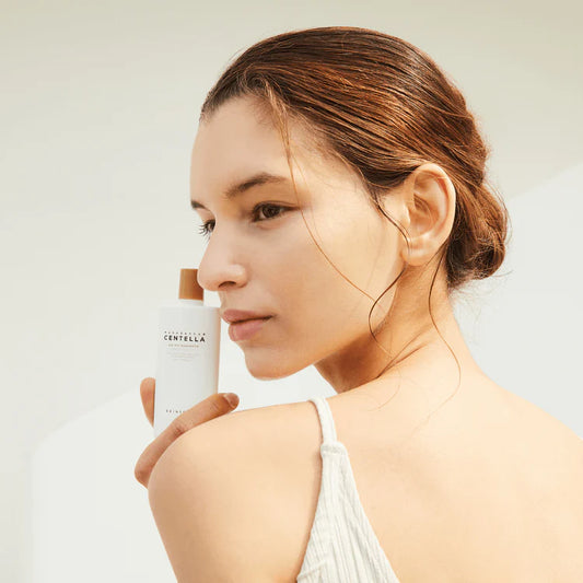 A woman holding SKIN1004 Centella Air-Fit Suncream Plus SPF50+ against a light background.